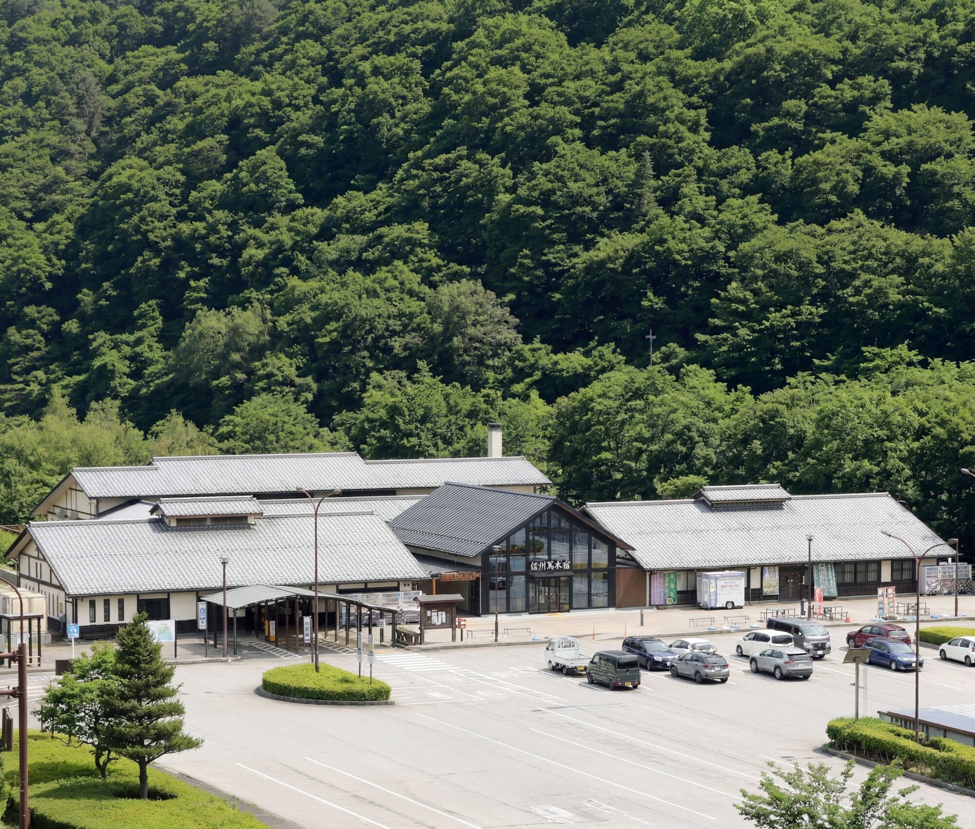 道の駅 信州蔦木宿 外観 緑豊かな山を背景に佇む瓦屋根と三角屋根が特徴的な「道の駅 信州蔦木宿」の建物外観と駐車場